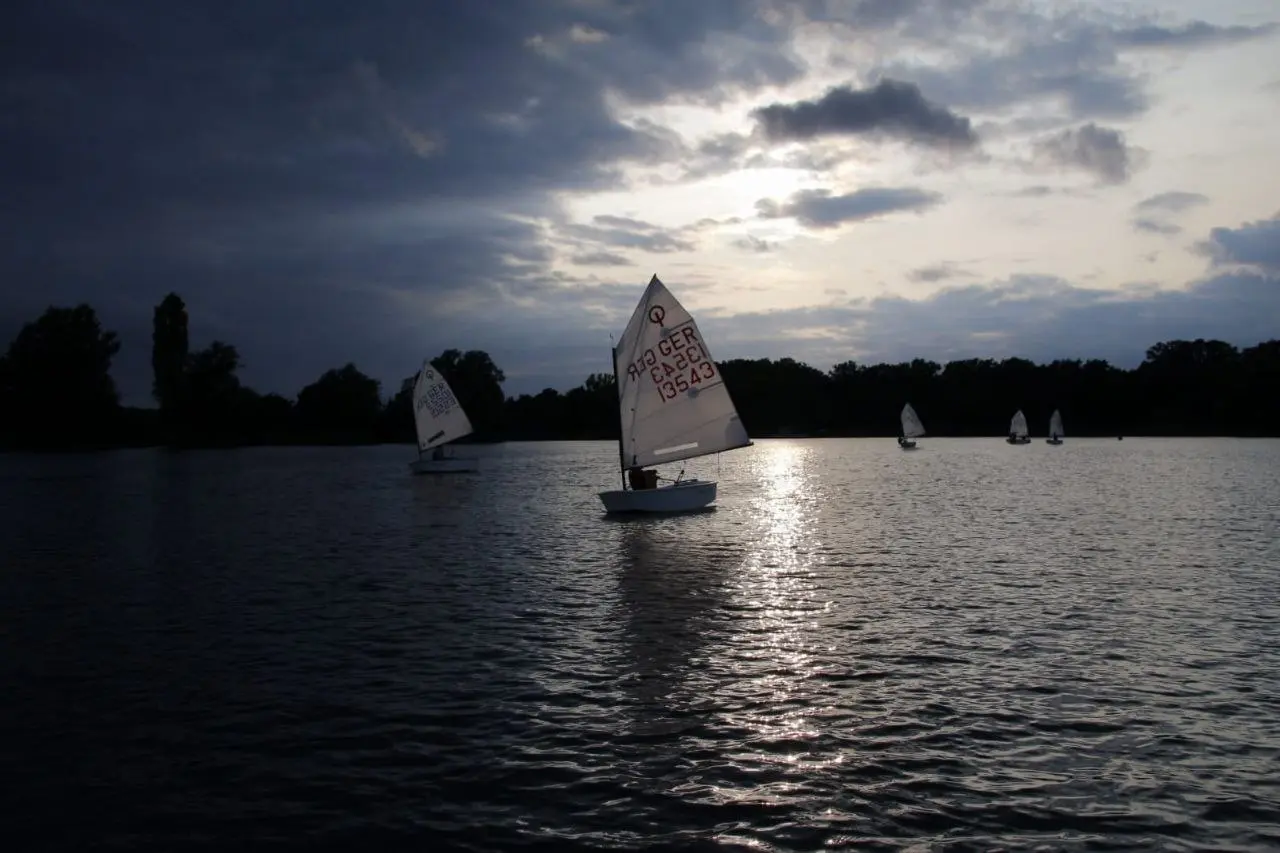 Optimist-Jolle im Gegenlicht auf dem See unter dunklen Wolken